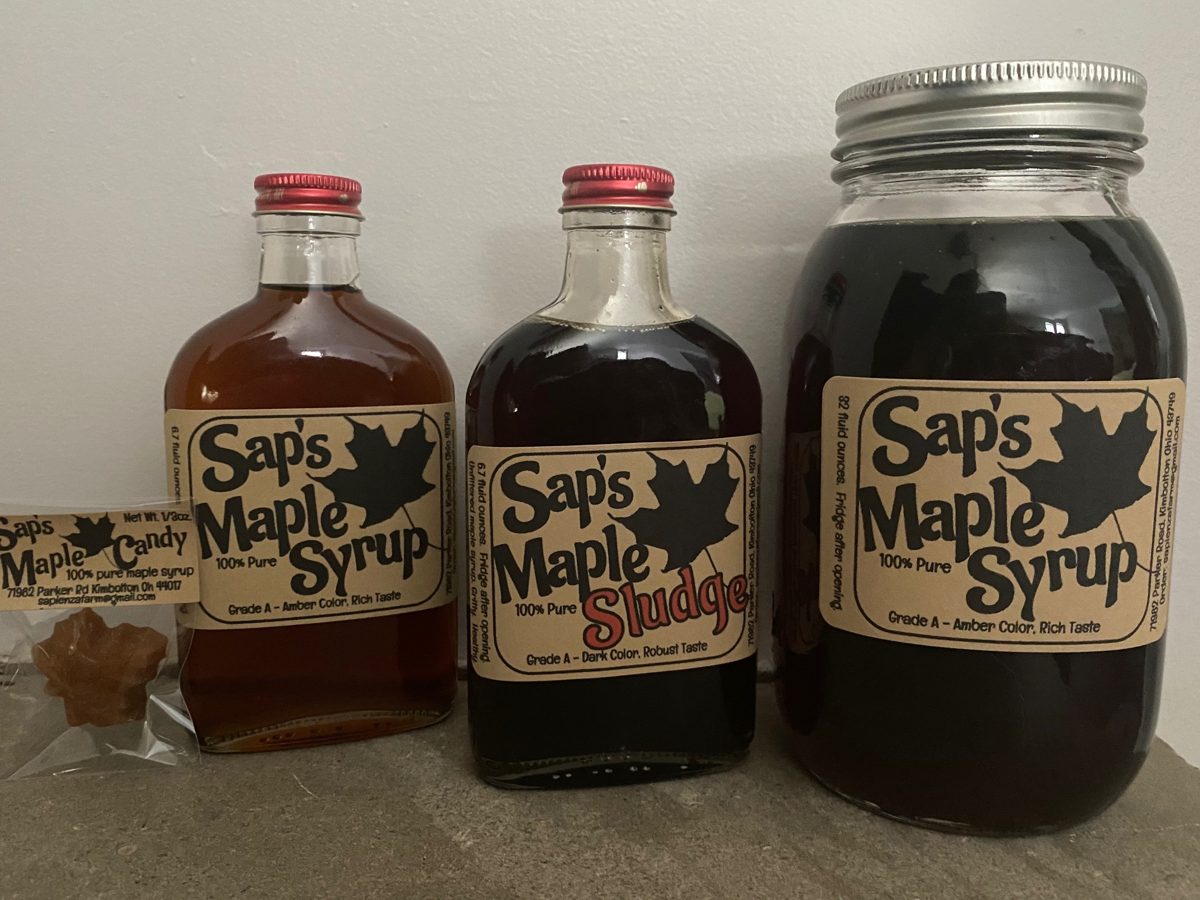 Sap's Maple Syrup in two flask bottles and a large jar, one filled with dark Maple Sludge, next to a bag of maple candy