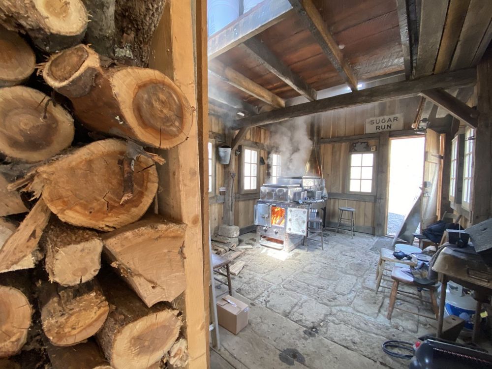 Inside the sugar house with the evaporator at the back and firewood in the foreground