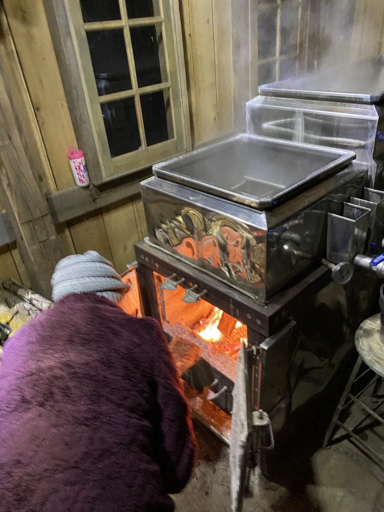 A person in a knit cap tending the fire under the evaporator